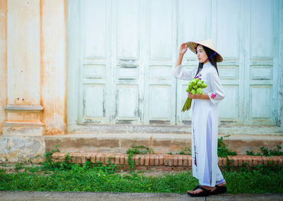 Side view of young woman holding buds against building