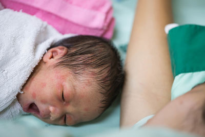 Close-up of baby boy sleeping by mother on bed in hospital