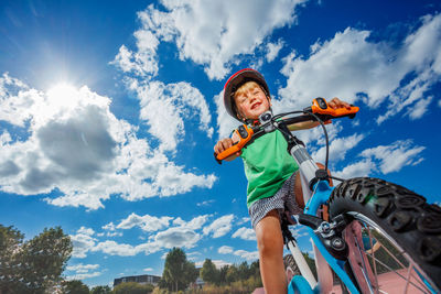 Low angle view of young woman riding bicycle against sky