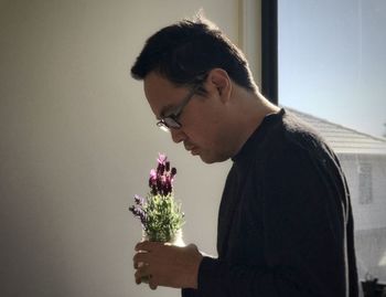 Side view of young man holding flower against wall