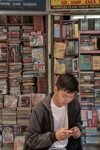 Young man using mobile phone while standing in bookstore