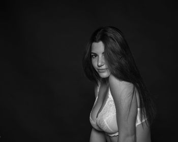 Portrait of woman in bra sitting against black background