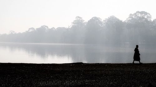 Silhouette man standing by water against sky