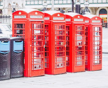 Red telephone booth on sidewalk by building in city