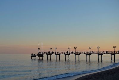 Silhouette wooden posts in sea against clear sky