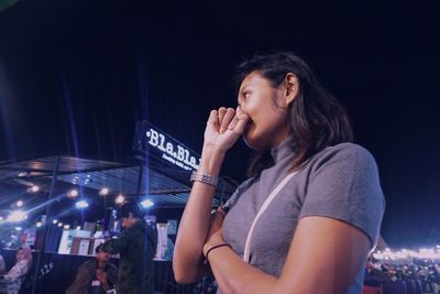 Smiling young woman looking at illuminated music concert at night