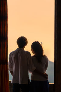 Rear view of couple standing against sky during sunset