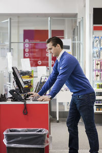 Salesman using computer while leaning on counter in store