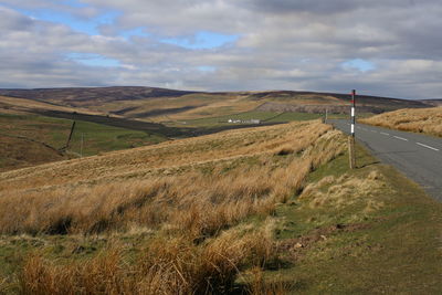 Scenic view of empty road on a moor, against a sunny/cloudy sky