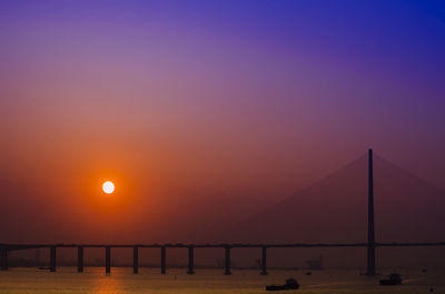 Silhouette bridge over sea against sky at sunset