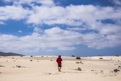 Rear view of teenage boy walking at desert against cloudy sky