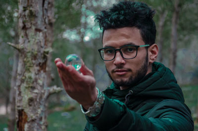 Portrait of young man holding crystal ball in forest