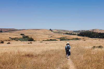 Woman in a hat walking outdoors through the hills with dry grass, view from the back