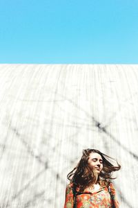 Young woman with eyes closed standing against wall