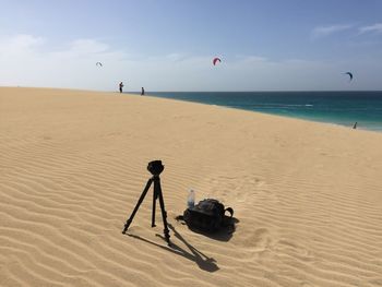 Camera on tripod with bag at beach against sky