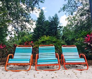 Empty chairs on beach against trees