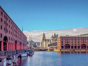 Historic buildings by river against blue sky