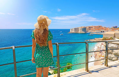 Rear view of woman standing by railing against sea