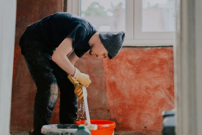 A young man washes window frames with water and a sponge.