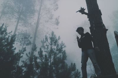 Man standing by tree in forest during foggy weather
