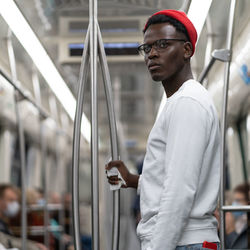 Portrait of thoughtful black student man in red hat holding handrail with napkin in subway train.