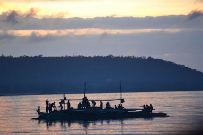 Silhouette people on boat against sky during sunset