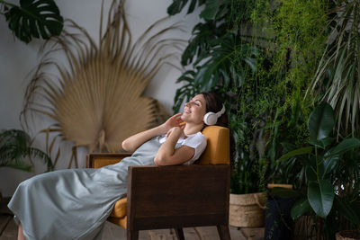 Smiling girl in headphone relax listen to music happy to have indoor garden with plants at home
