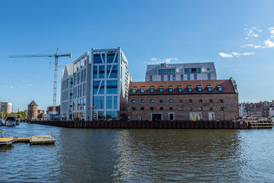 View of buildings by river against blue sky