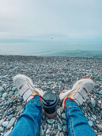 Low section of person by sea against sky