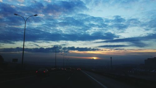 Cars on road against sky at sunset