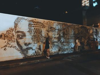 Full length of woman standing against graffiti wall at night