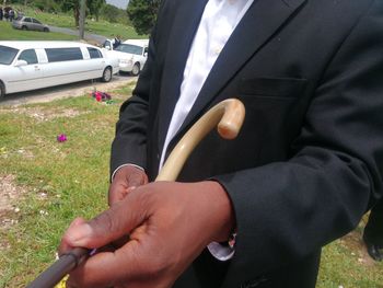 Midsection of man holding hands on car while sitting on field