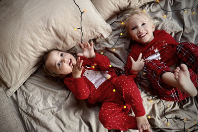 High angle view of cute sisters lying on bed