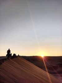 Silhouette people riding on desert against sky during sunset