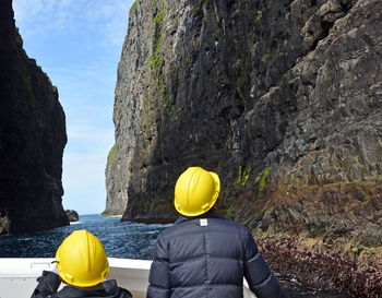 Rear view of people standing by rocks against sky