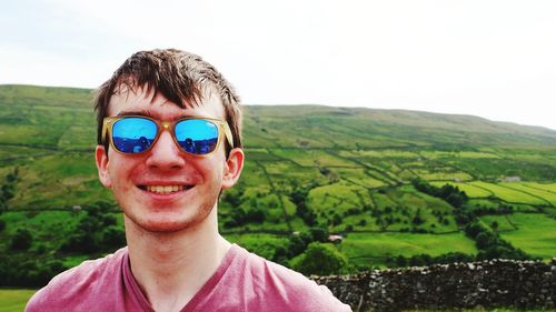 Portrait of smiling young man wearing sunglasses with landscape in background