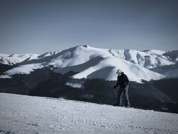 Rear view of man standing on snowcapped mountain against sky
