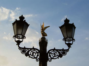 Low angle view of lamp post with statue in background against sky