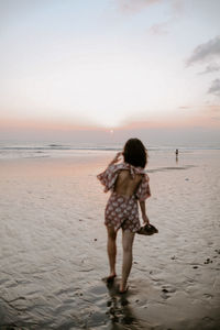 Rear view of girl standing at beach against sky
