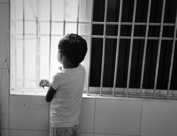 Rear view of boy standing by window at home