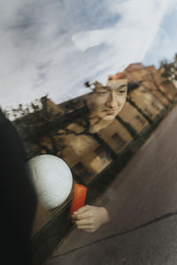 Contemplative teenage boy with soccer ball seen through car window