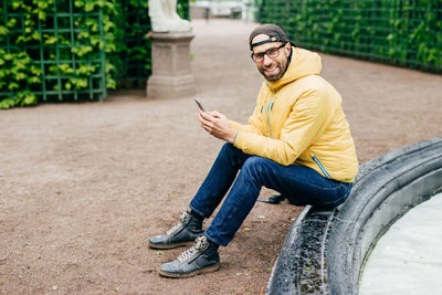 Full length of young man sitting on mobile phone