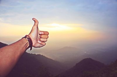 Cropped hand of person gesturing thumbs up sign against sky