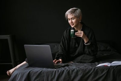 Woman working at home with laptop, drinking coffe, black colors interior