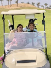 Two young girls driving a golf cart on a golf course while having a blast. 