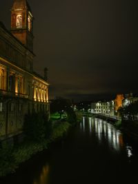 Illuminated buildings by river against sky at night