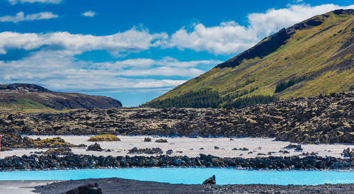 Scenic view of sea by mountain against sky