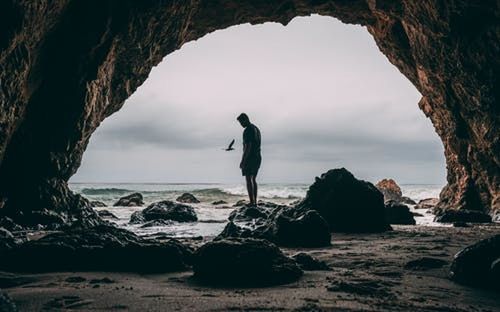 Silhouette of man standing on rock by sea against sky