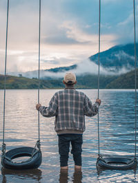 Rear view of man standing by swing in lake