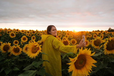 Man and yellow sunflower on field against sky during sunset